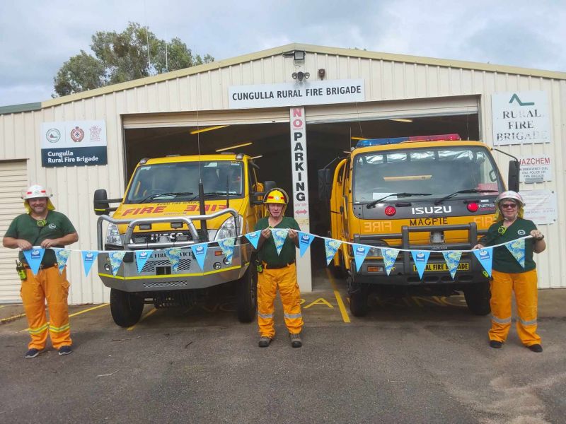 Three firemen standing in front of two trucks holding up Ergon Energy bunting