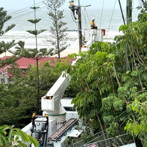 Crews in cherry picker working on powerlines with ocean in background