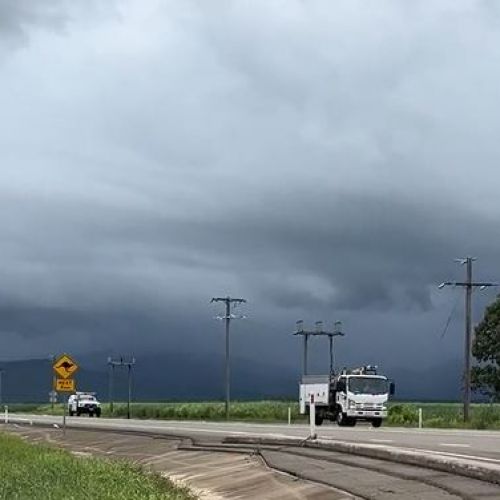 Crews on road accessing powerlines with black rain clouds in distance