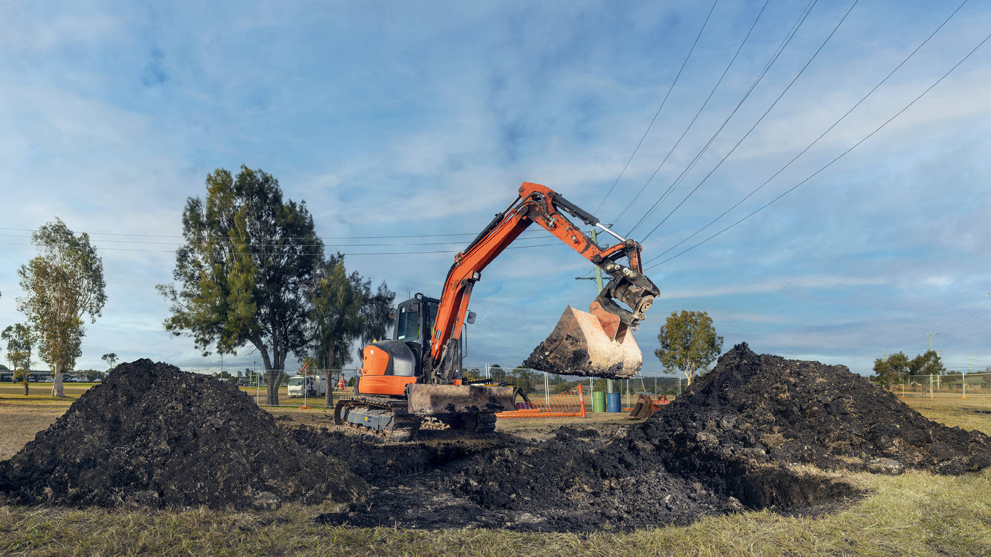 Orange excavator digging under powerlines