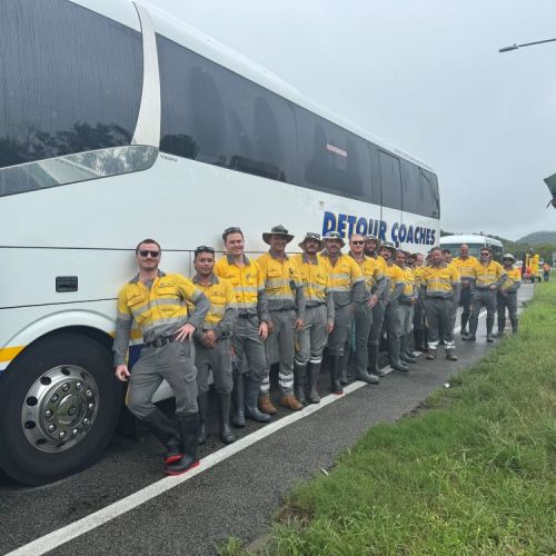 A number of crew members leaning against a coach on side of road