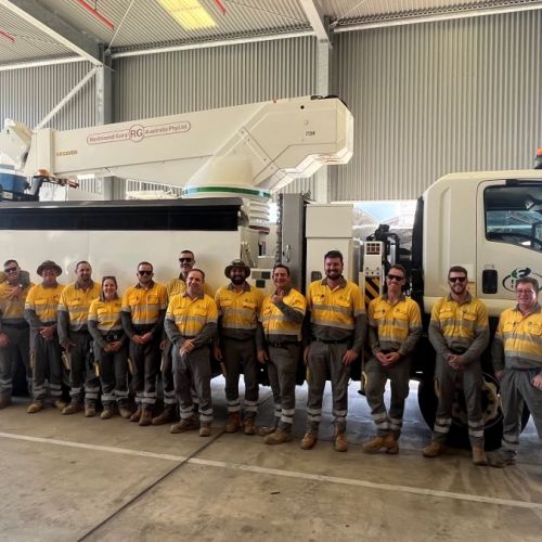 Group photo in a warehouse with a truck in background of crews