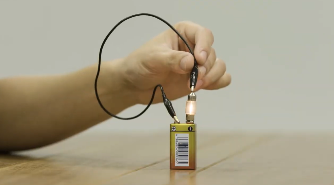 A person with a battery and conductor to show how a light works